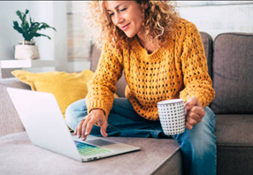 woman in yellow shirt on laptop holding a coffee cup